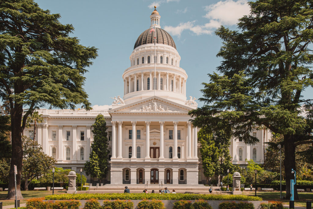 Photo of the California state Capitol building, with white stone columns and a dome.